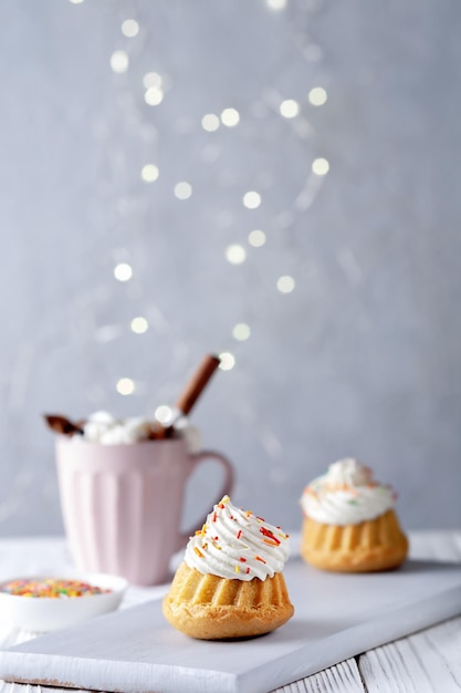 Vanilla muffins with cream cheese cream and caramel sprinkles on a wooden background copy space