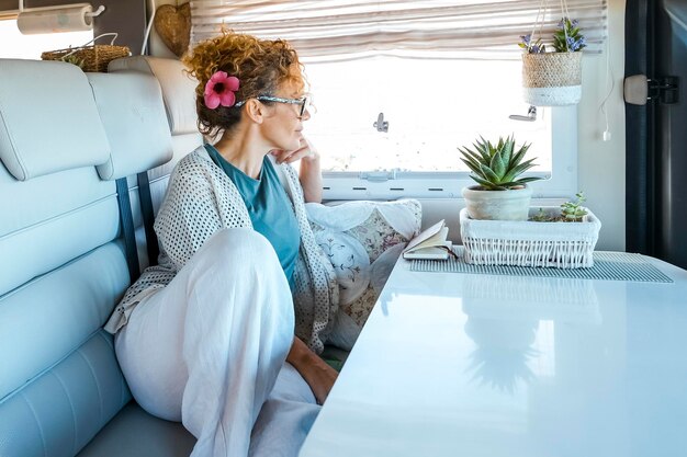 Photo vanlife people lifestyle one young adult female relax on the sofa inside a modern cozy motorhome camper van and looking outside the window travel people lifestyle renting rv vehicle for vacation