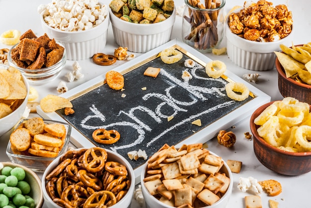 Photo variation different unhealthy snacks crackers, sweet salted popcorn, tortillas, nuts, straws, bretsels