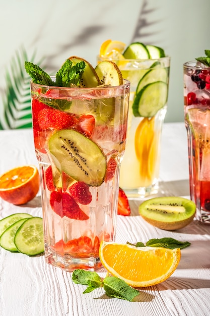 Variations of lemonades with different fruits and syrups on wooden table under morning sun