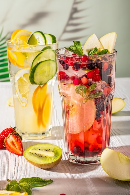 Variations of lemonades with different fruits and syrups on wooden table under morning sun