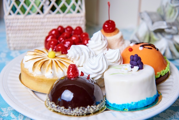 A variety of cakes on a white plate stand on a decorated table.