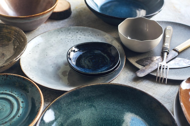 Variety of ceramic tableware plates bowls glazed dishes and cutlery on stone table selective focus