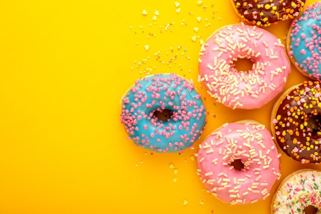 Variety of colorful tasty glazed donuts on a colored