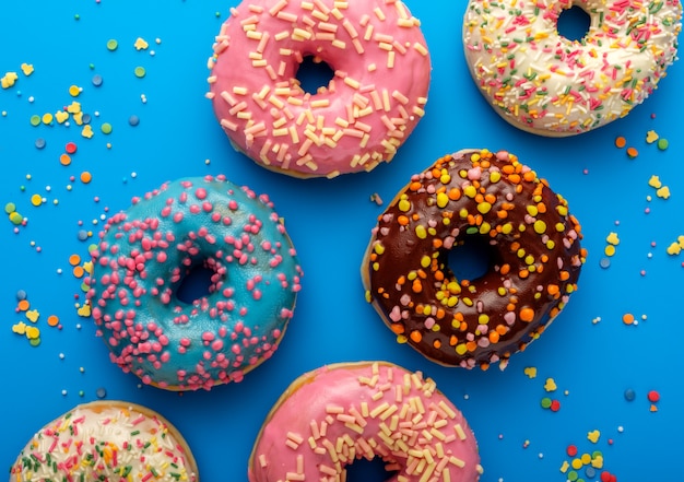 Variety of colorful tasty glazed donuts on a colored