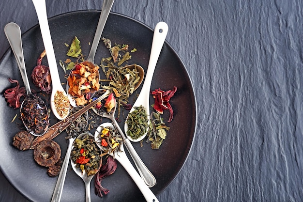 Variety of dry tea in white spoons on grey background closeup