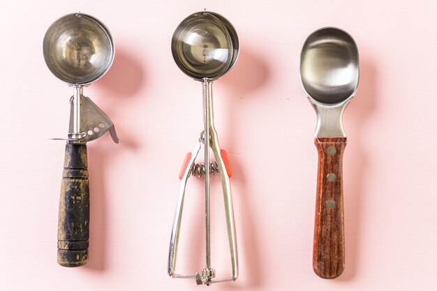 Variety of empty metal ice cream scoops on pink background.