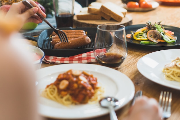 Variety of food on the wooden table and friends eating dinner together.