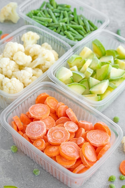 A variety of frozen vegetables in plastic containers on a gray concrete background Healthy food