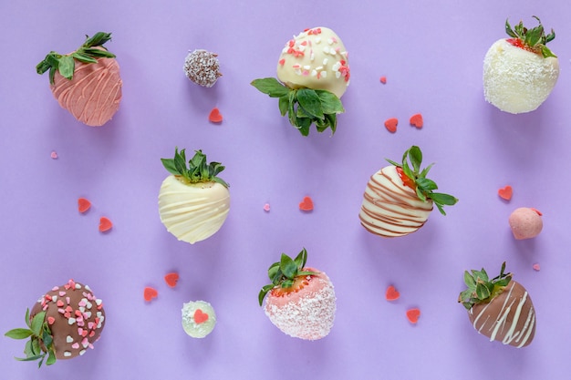 Variety of handmade chocolate covered strawberries with different toppings on purple background