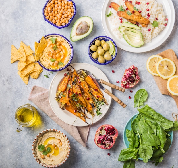 Variety of healthy vegan snacks, gourmet dips. Hummus,  roasted carrots, rice with tempeh in ceramic bowls viewed from above, plant based food