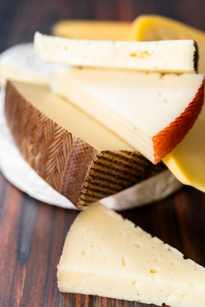 Variety of large gourmet cheese wedges on a dark wooden background.