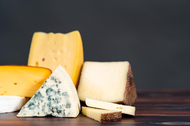 Variety of large gourmet cheese wedges on a dark wooden background.