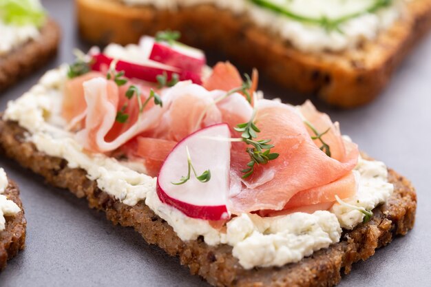 Variety of mini sandwiches with cream cheese, vegetables and salami.