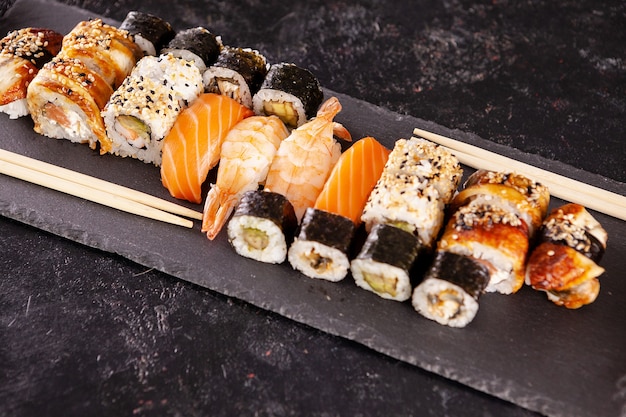 Variety mix of different types of sushi on dark stone background