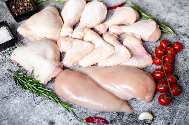 A variety of raw chicken legs are on a table with a metal pan and a red pepper.