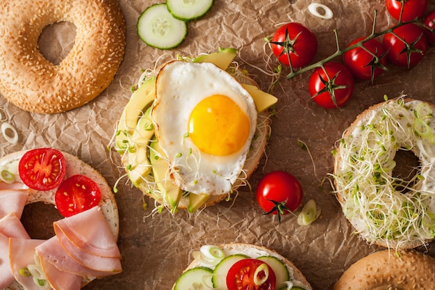 Variety of sandwiches on bagels: egg, avocado, ham, tomato, soft cheese, alfalfa sprouts