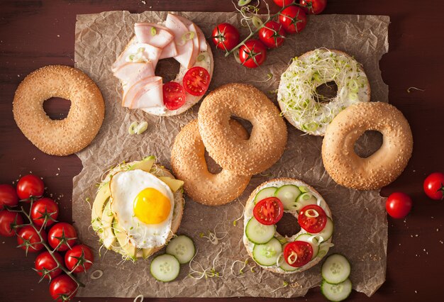 Variety of sandwiches on bagels: egg, avocado, ham, tomato, soft cheese, alfalfa sprouts