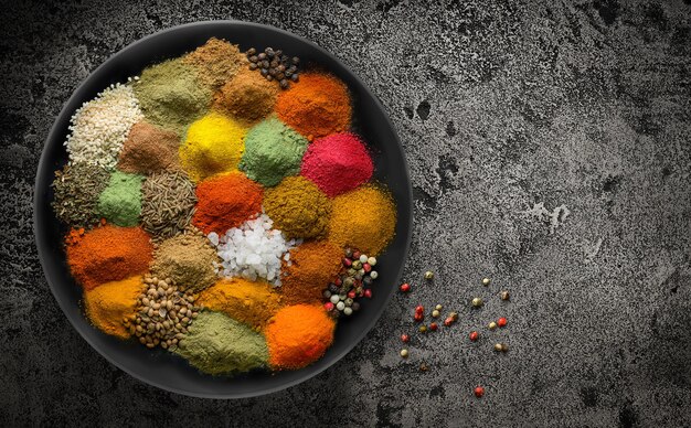 Variety of spices and condiments on black plate on black stone grunge background Copy space