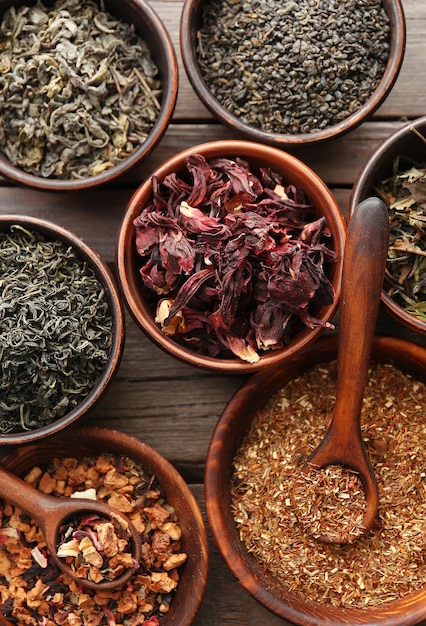 Variety of tea in round bowls with spoon on wooden table top view