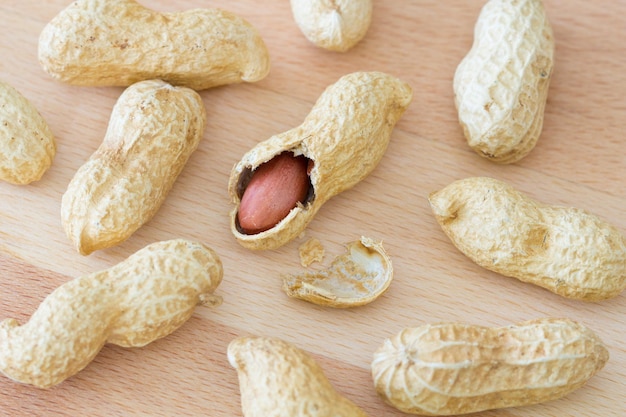 Variety of whole peanuts and one half peeled peanut with cracked shell on a wooden table