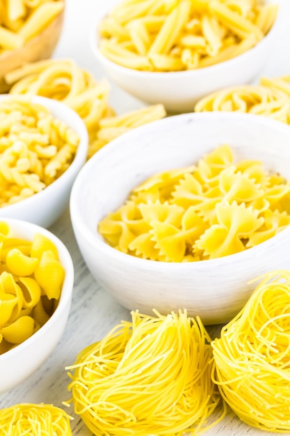 Variety of yellow dry pasta in small round bowls.