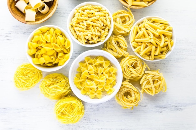 Variety of yellow dry pasta in small round bowls.