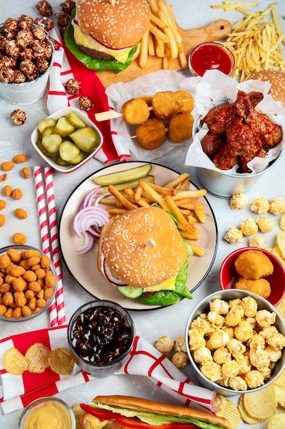 Various of american food French fries hamburgers nuggets hotdog chips popcorn sauces on a white background top view