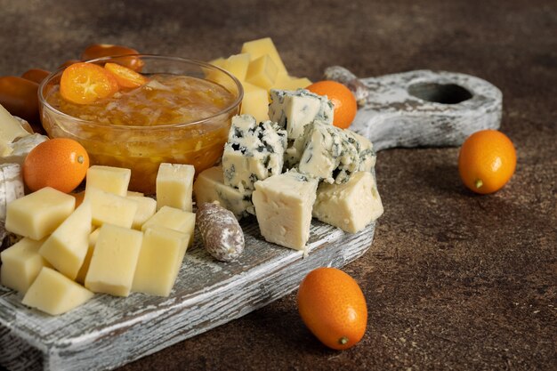 Photo various cheeses and kumquat fruits on the old wooden board on wooden table