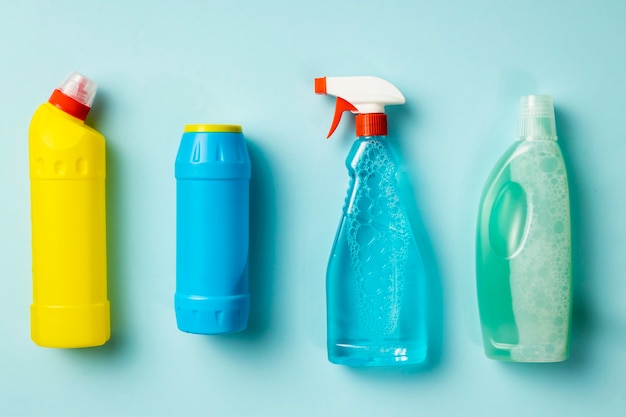 Various cleaning supplies, sprays and bottles on blue background, top view. House cleaning concept