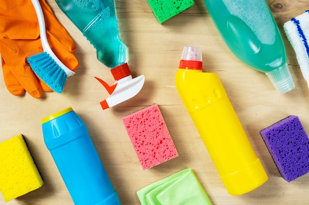 Various cleaning supplies, sprays, bottles, sponge, rubber gloves on wooden background, top view. Cleaning concept