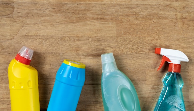 Various cleaning supplies, sprays and bottles on wooden background, top view. Cleaning concept