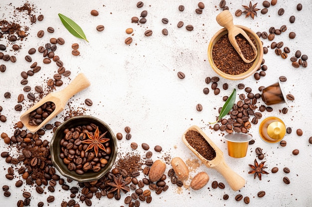 Photo various coffee , dark roasted coffee beans , ground and capsules with scoops setup on white concrete