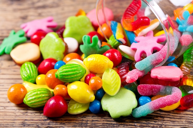 Various colorful candies, jellies and marmalade in glass jar on wooden table