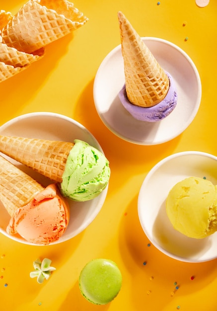 Various colorful ice cream scoops or balls with waffle cones on yellow background Top view