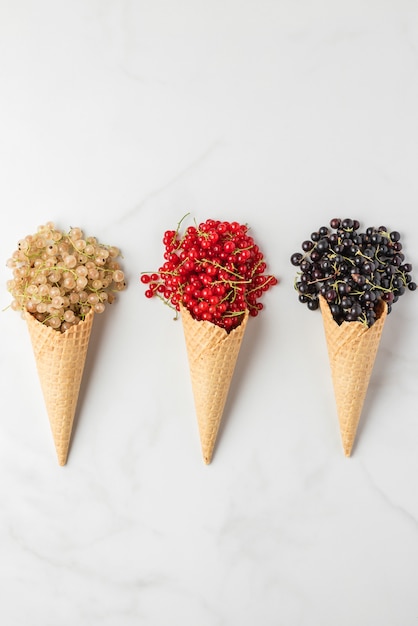 Various currant berries in waffle ice cream cones on white marble. Red, black and white currant. top view