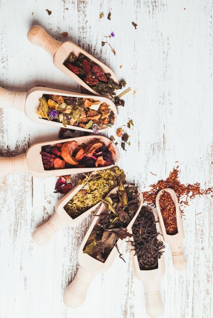 Various of dried tea in wooden scoops on white shabby table