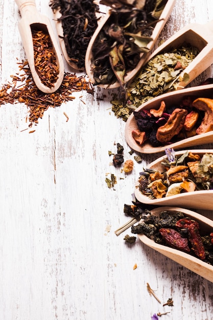 Various of dried tea in wooden scoops on white shabby table