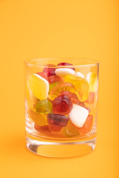 Various fruit jelly candies in drinking glass on orange background close up side view