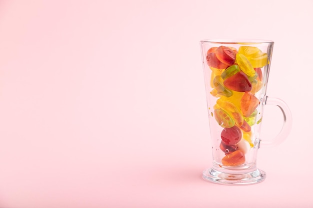 Various fruit jelly candies in drinking glass on pink background copy space side view