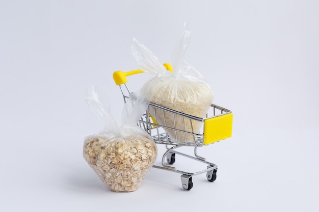 Various groats in packages in a grocery cart on a white background. Rice and oatmeal