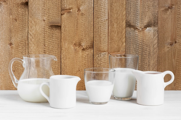 Various jugs and glasses with milk on the wooden table