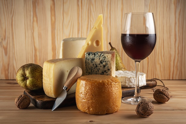 Various kind of cheese with glass of wine on wooden table.