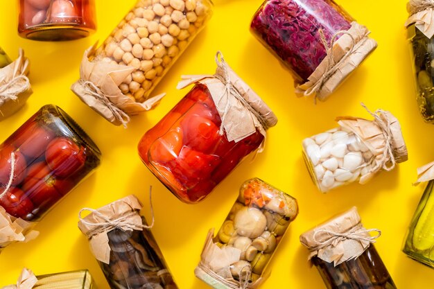 Photo various kinds preserves vegetables and mushroome in glass jars placed on yellow background top view flat lay