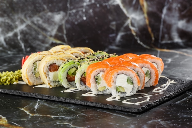 Various kinds of sushi served on black marble background. Sushi menu for Japanese food. Japanese sushi set. Rolls with tuna, salmon, shrimp, crab, caviar and avocado. Horizontal photo.