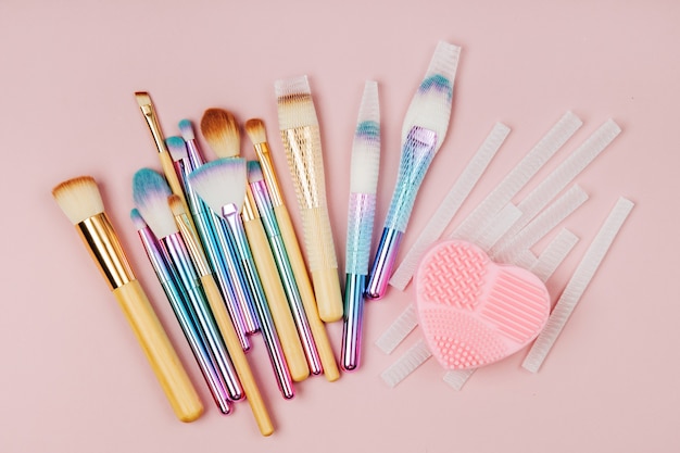 various makeup brushes with brush cleansing pad and brush guard on a pastel pink background