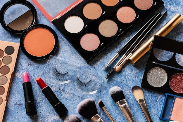 Various makeup products, brushes on blue background