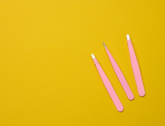 Various metal eyebrow tweezers on a yellow background, top view