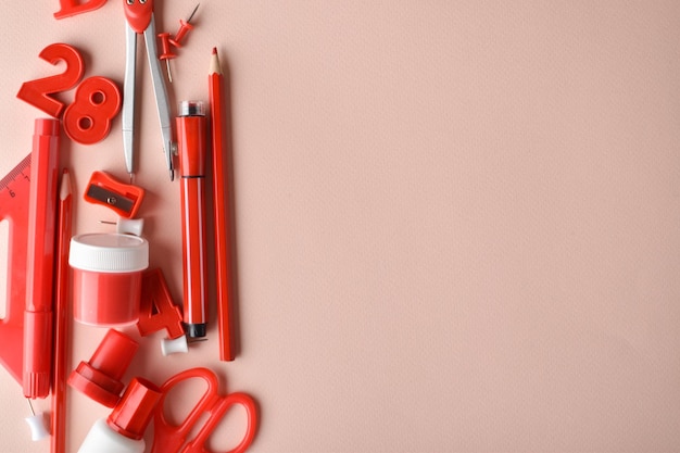 Various office supplies of red color lie on the side on a beige background