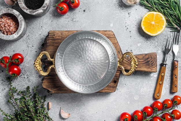 Various organic spices herbs and ingredients around empty aged cooking skillet Gray background Top view Copy space